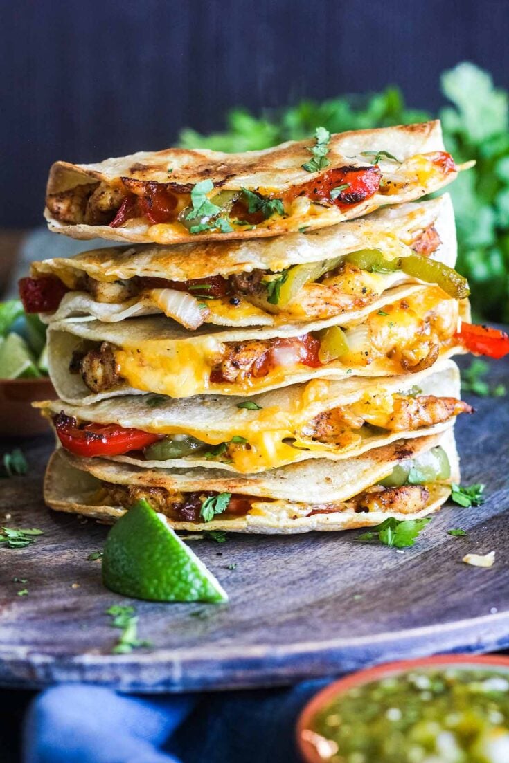 https://goodfoodbaddie.com/wp-content/uploads/2022/07/Stack-of-crispy-chicken-fajita-tacos-with-a-bowl-of-salsa-and-bunch-of-cilantro.-735x1103.jpg