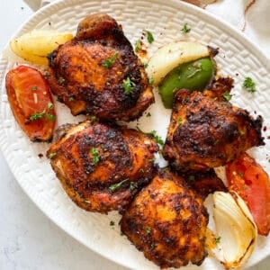 Plate of four crispy chicken thighs alongside roasted vegetables