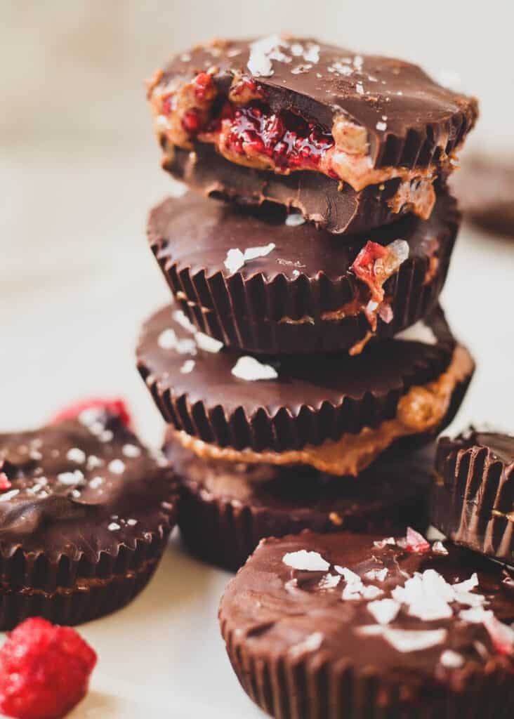 stack of dark chocolate almond butter cups with raspberry with the almond cup on the top showing the inside filling of raspberry jam and almond butter