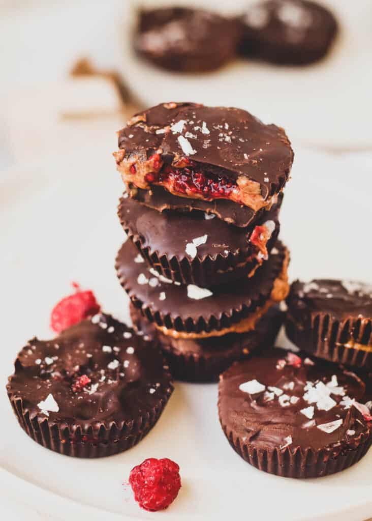 stack of dark chocolate almond butter cups with raspberry with the almond cup on the top showing the inside filling of raspberry jam and almond butter