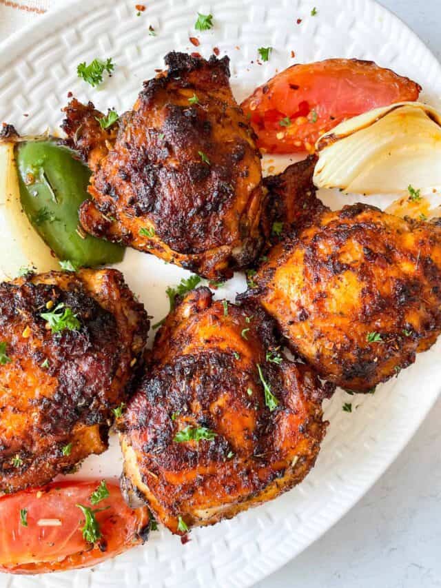 four bone-in air fryer chicken thighs on a plate with peppers onions and tomatoes