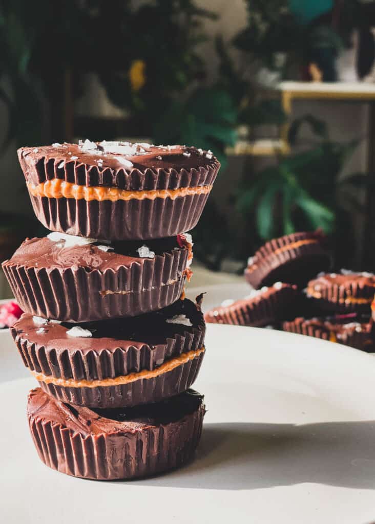 stack of dark chocolate almond butter cups with a plate of chocolate almond butter cups placed in the background