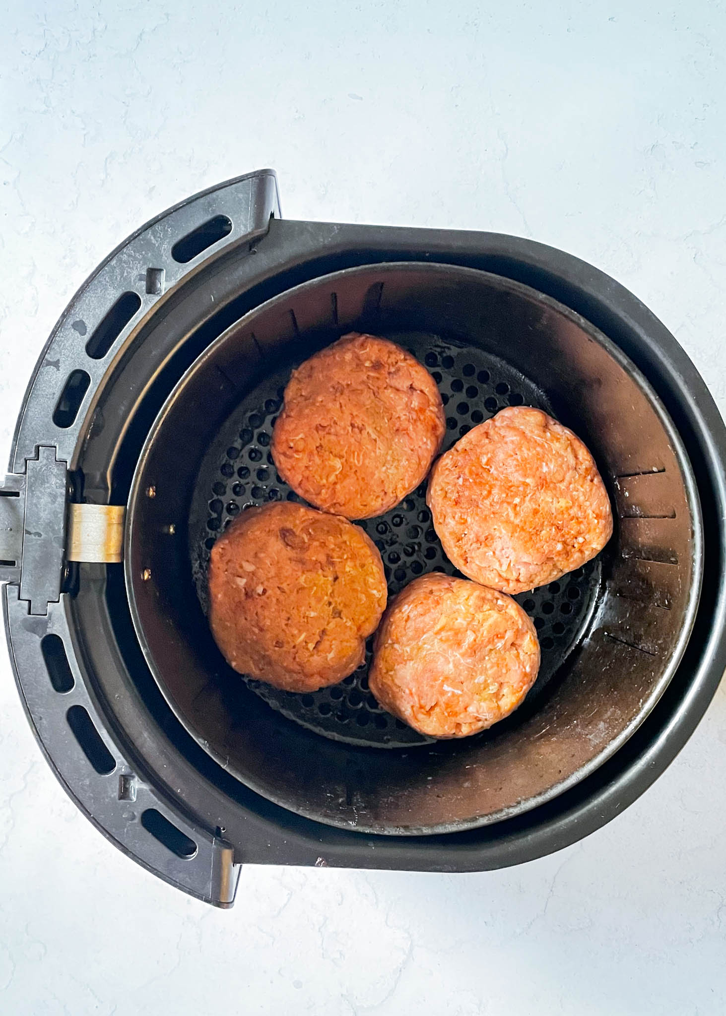 overhead view of four raw turkey burger patties placed in an air fryer