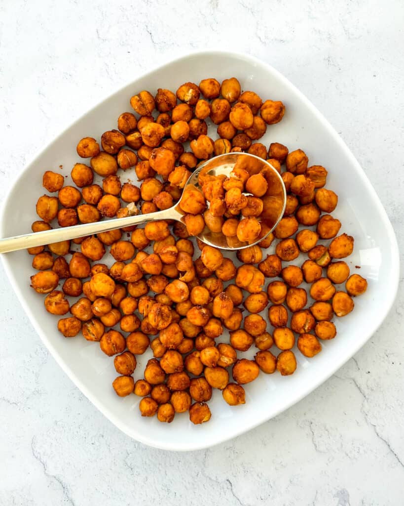chickpeas that have been made in an air fryer are on a small white plate with a gold spoon in the middle with some chickpeas on the spoon