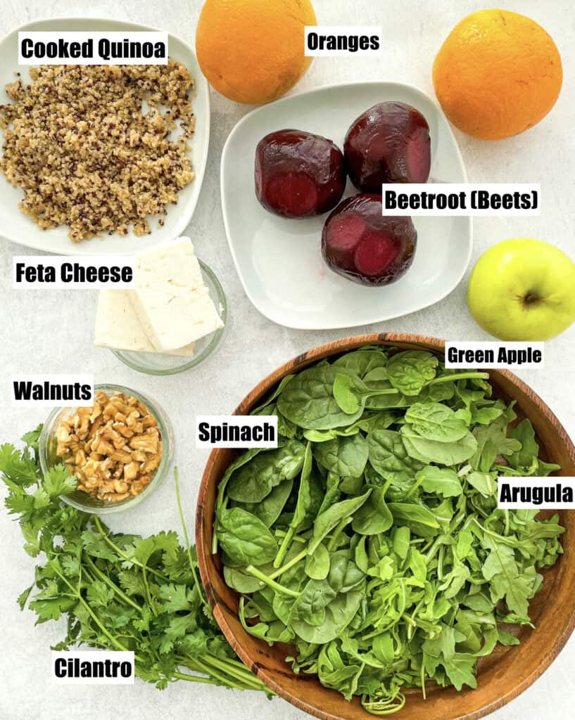 ingredients to make beetroot salad shown are cooked quinoa oranges apple cooked beets feta cheese walnuts cilantro feta cheese and spinach and arugula in a wooden bowl