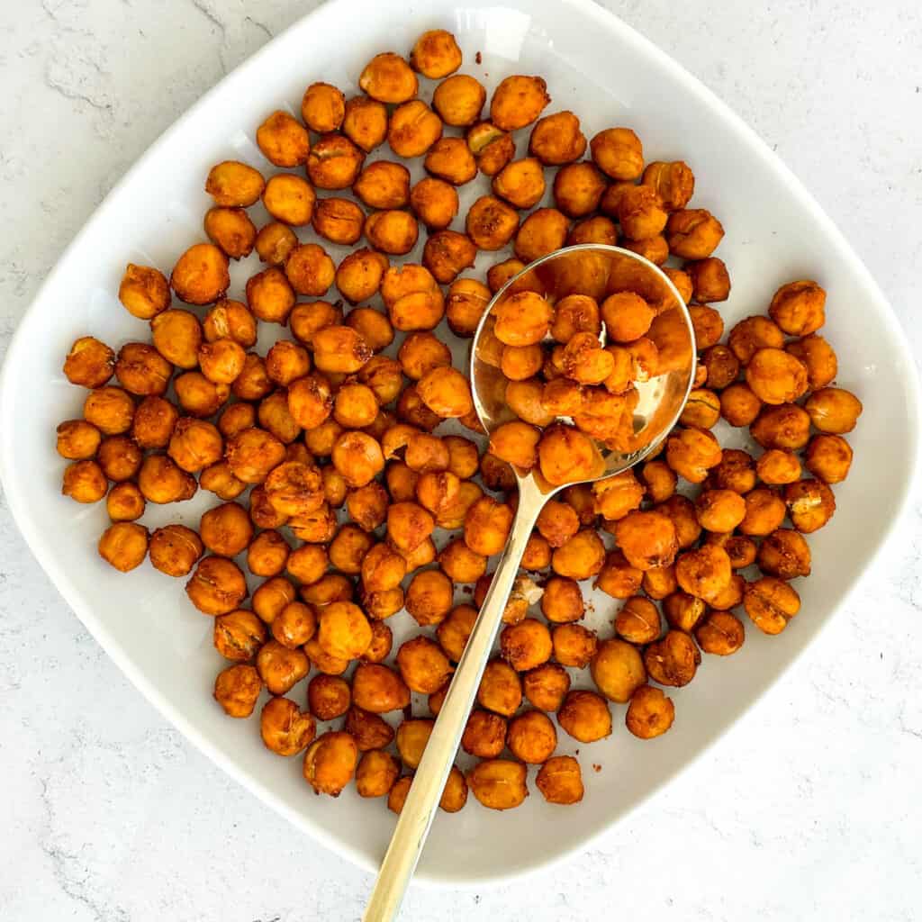 chickpeas that have been made in an air fryer are on a small white plate with a gold spoon in the middle with some chickpeas on the spoon