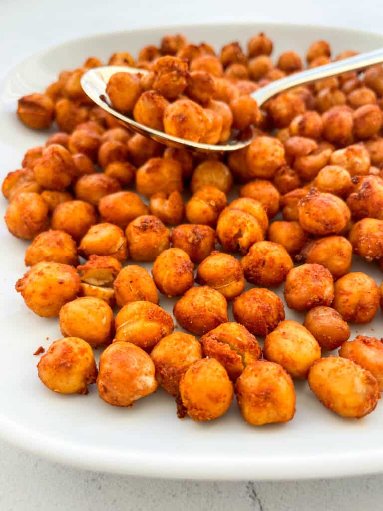 chickpeas that have been made in an air fryer are on a small white plate with a gold spoon in the middle with some chickpeas on the spoon