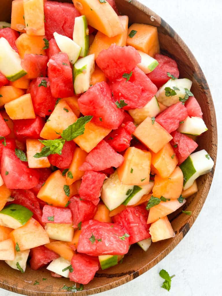 watermelon cantaloupe cucumber salad with honey lime mint dressing in a large wooden bowl 