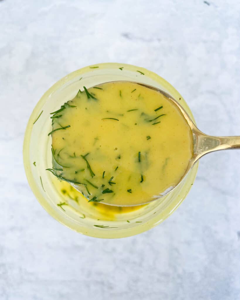 close up of honey dijon dill vinaigrette on a large golden spoon with mason jar underneath of spoon