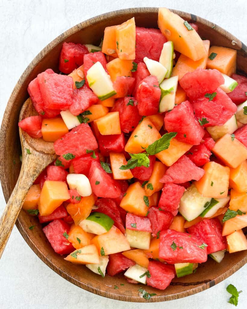 watermelon cantaloupe cucumber salad with honey lime mint dressing in a large wooden bowl with a wooden spoon in the bowl