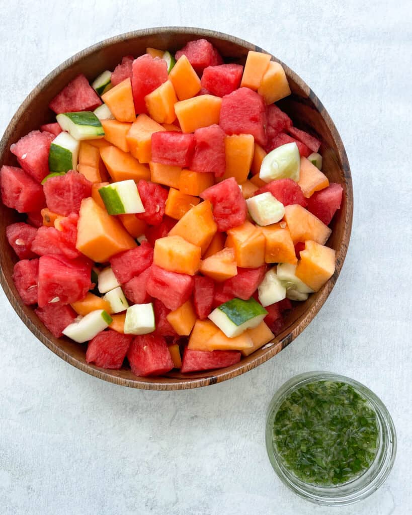 watermelon cantaloupe cucumber salad with honey lime mint dressing in a large wooden bowl with a small bowl of honey lime dressing on the side