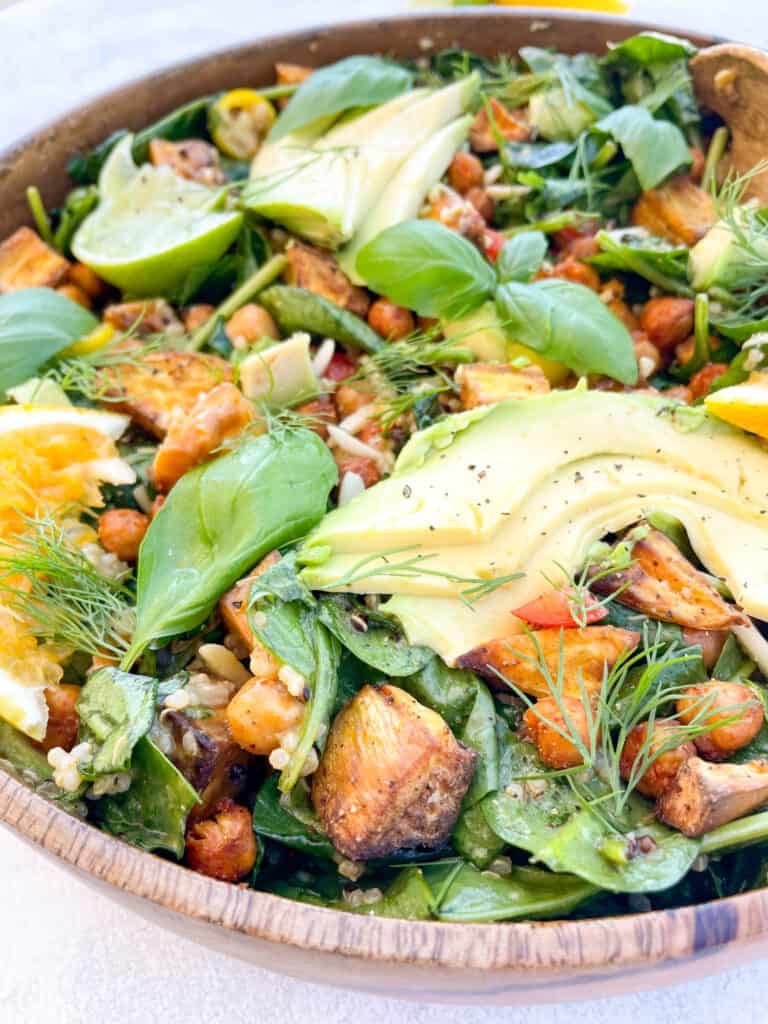 close up of salad with roasted sweet potatoes avocado basil and orange on top