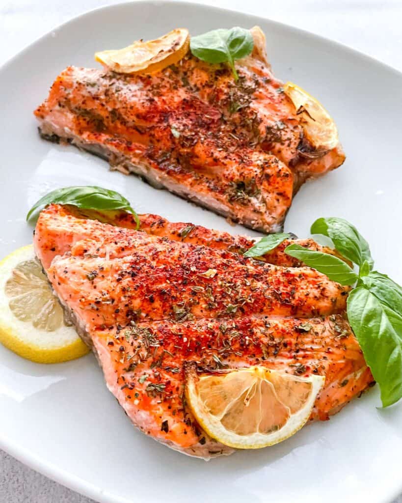 two salmon fillets on a plate with slides lemon and fresh basil