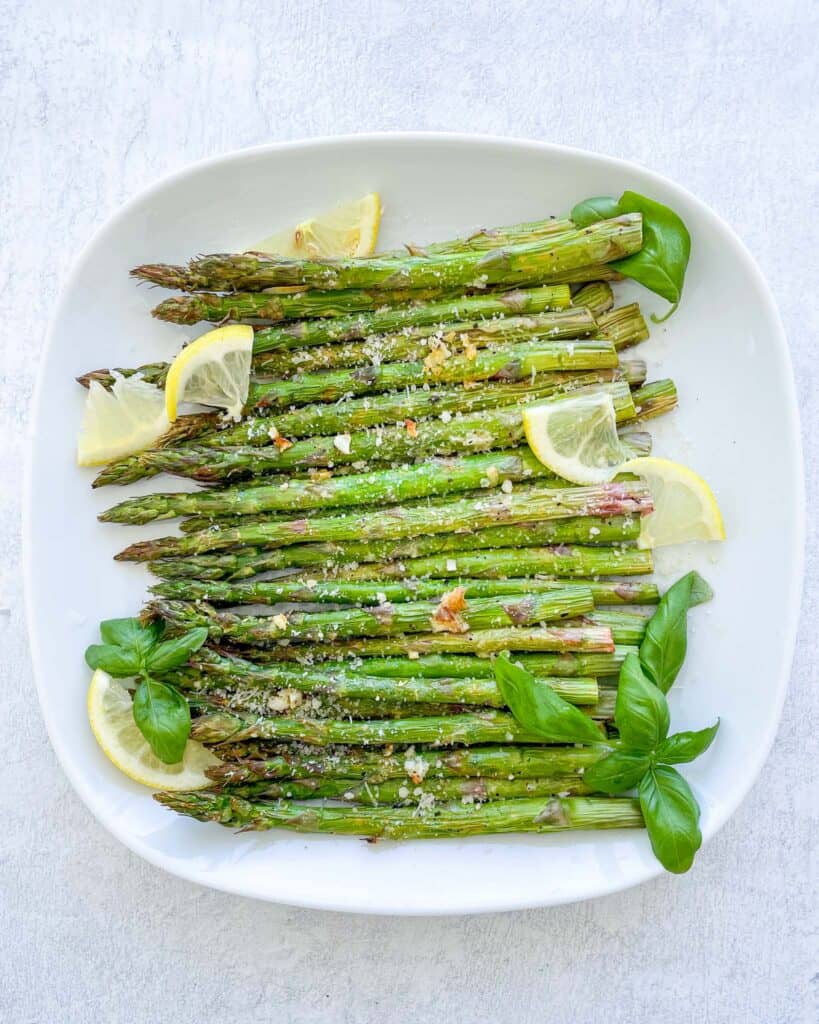 cooked asparagus on a white plate garnished with lemon and fresh basil