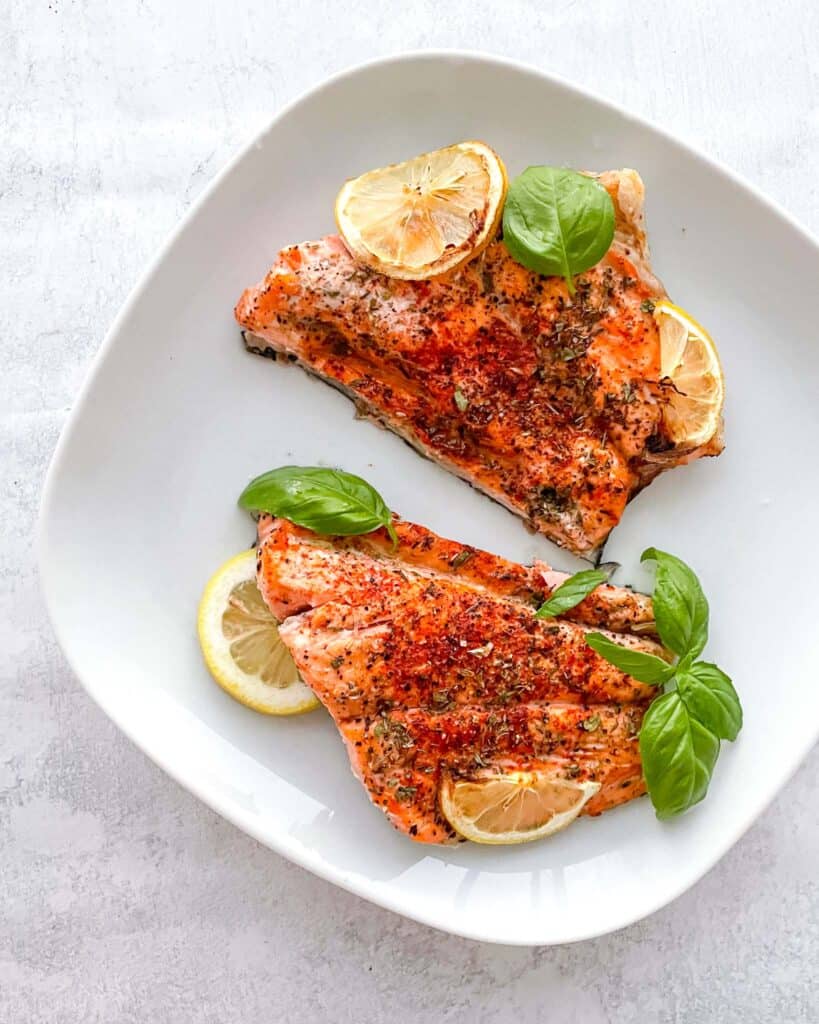 two salmon fillets on a plate with sliced lemon and garnished with basil