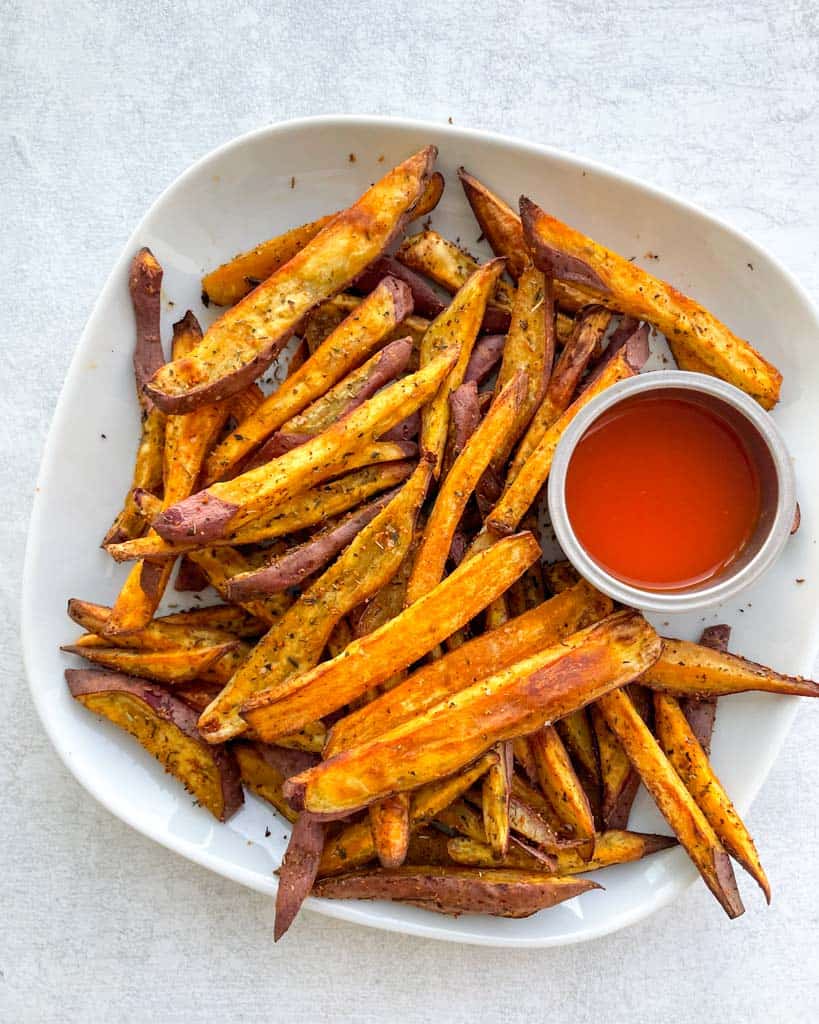 overhead view of a plate of sweet potato fries with a small dish of ketchup on the side