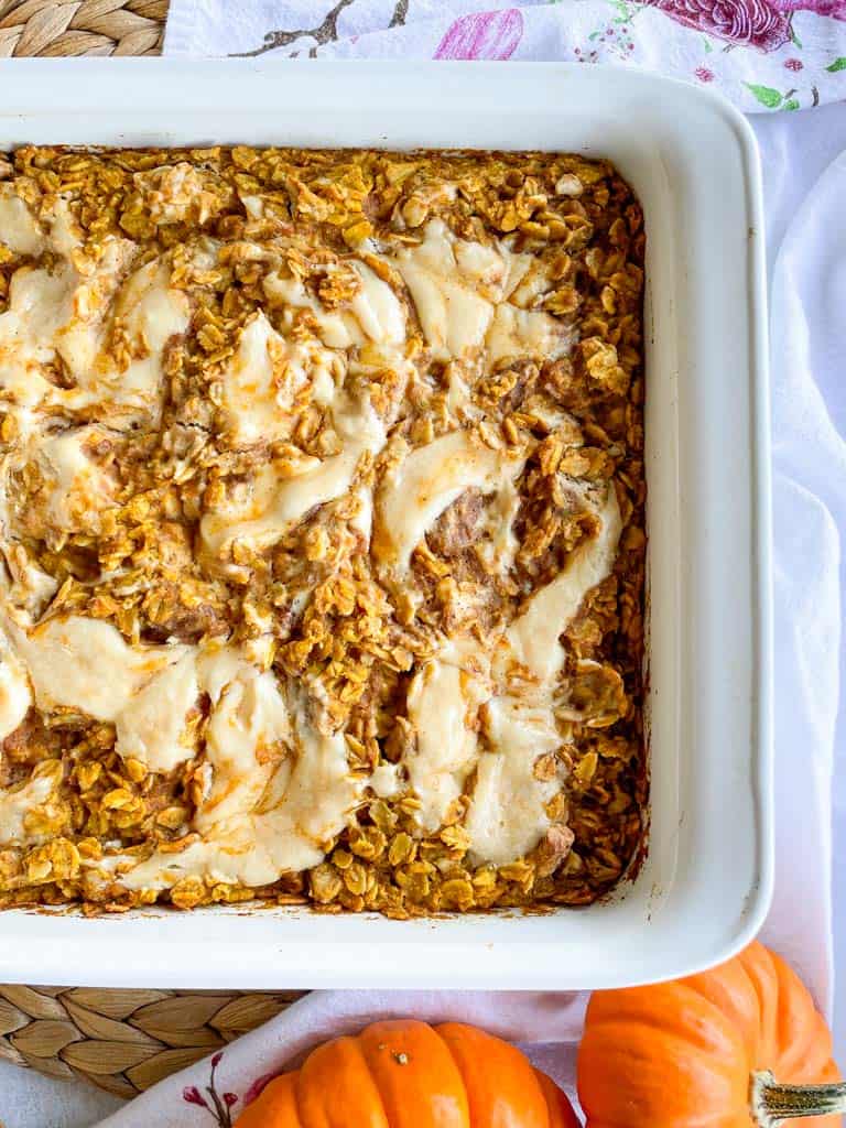 pumpkin baked oatmeal with maple cream cheese swirl in a white baking dish with small pumpkins in the corners of the photo