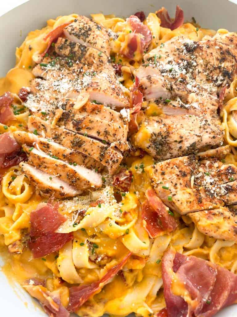 butternut squash pasta topped with crispy prosciutto and sauteed chicken and parmesan cheese in a skillet 