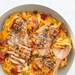 butternut squash pasta topped with crispy prosciutto and sauteed chicken and parmesan cheese in a skillet with a wooden spoon