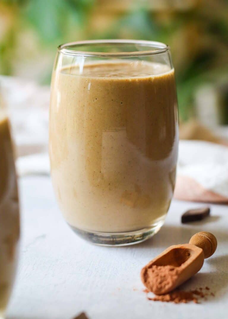 one full glass of chocolate zucchini smoothie this a scoop of raw cacao powder on a small spoon in front of the smoothie