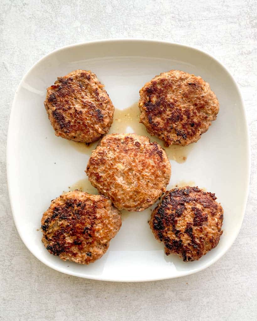 five fully cooked burger patties on a plate