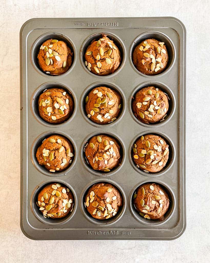pumpkin muffins topped with pumpkin seeds in a muffin tin