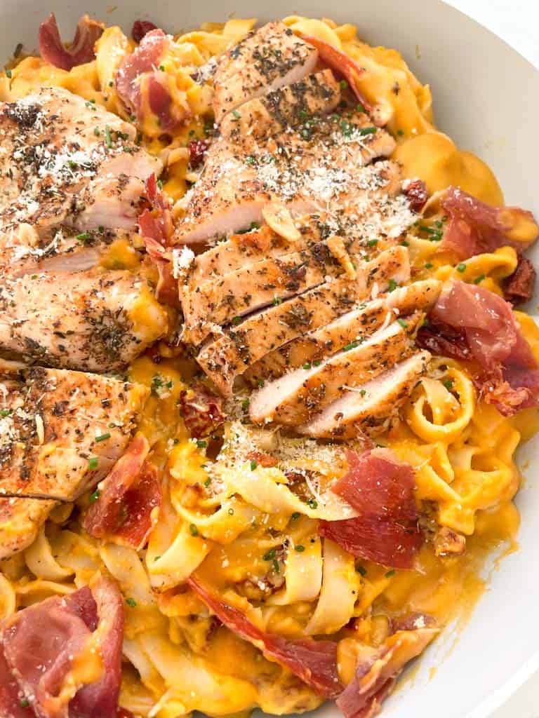 butternut squash pasta topped with crispy prosciutto and sauteed chicken and parmesan cheese in a skillet