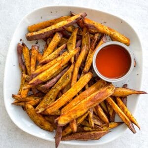 overhead view of a plate of sweet potato fries with a small dish of ketchup on the side