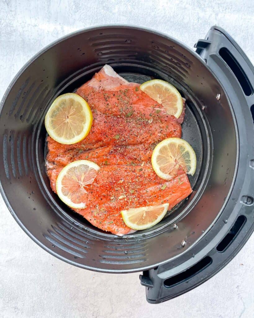 raw seasoned salmon topped with lemons placed in an air fryer