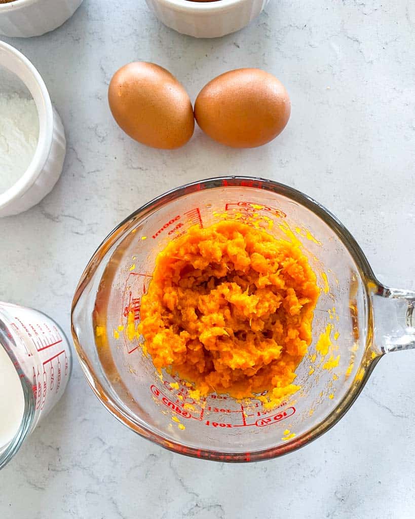 a measuring cup filled with sweet potato mash with two eggs beside it
