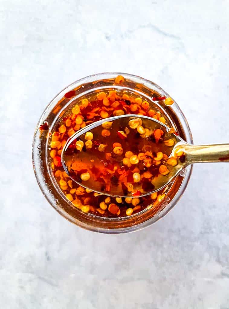 a spoon holding up hot honey sauce over a small jar