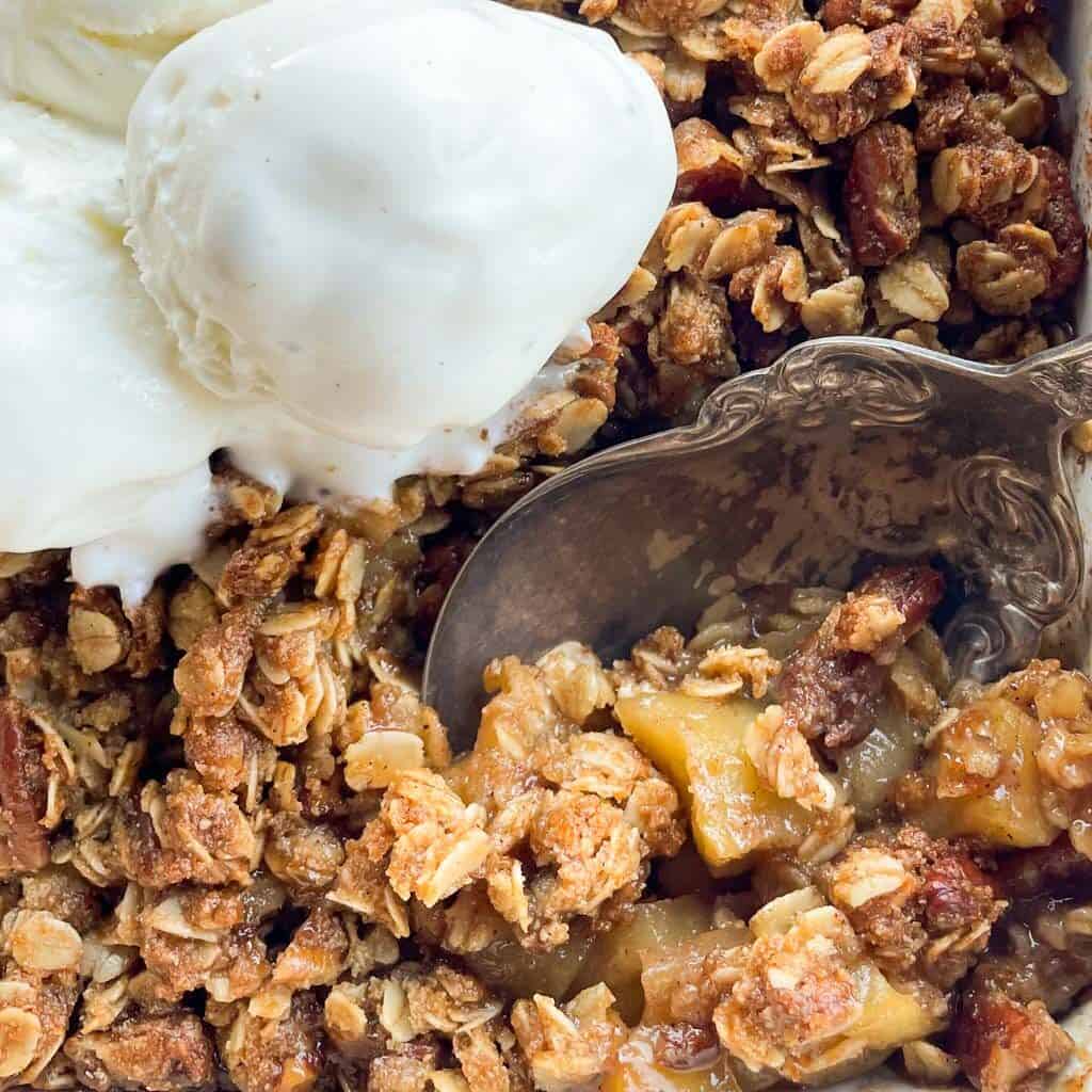 close up view of apple crisp with oats and a scoop of vanilla bean ice cream