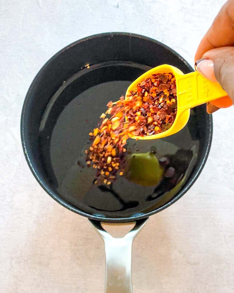 pouring red pepper flakes into a pot of honey