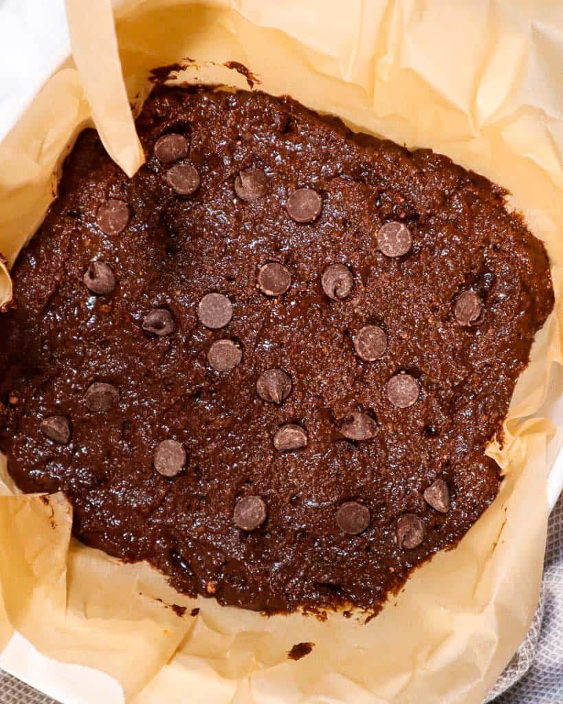 vegan chocolate chip brownie batter in a parchment lined baking dish before baking
