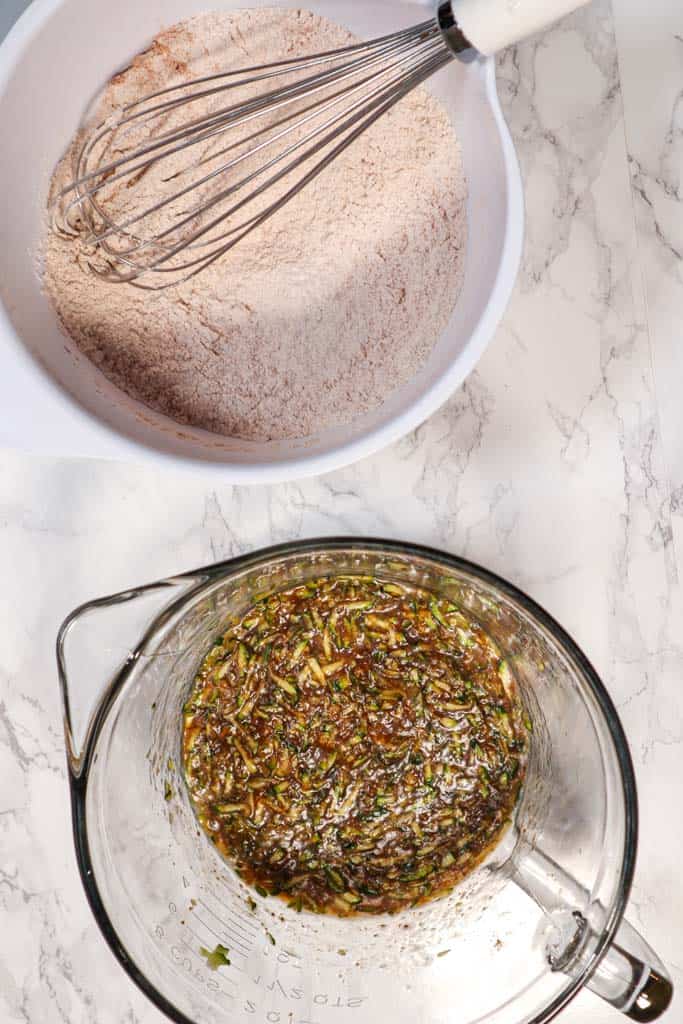 dry ingredients to make muffins in a white bowl with a whisk next to a glass bowl with the wet ingredients inside