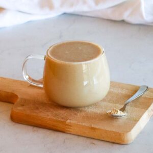 clear mug of maca coffee on a cutting board with a small spoon of maca powder on the side of the mug