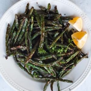 overhead view of a plate of green beans with lemon wedges on the side
