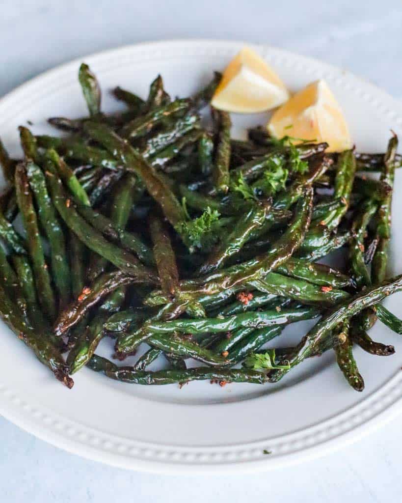plated air fryer green beans with two lemon wedges