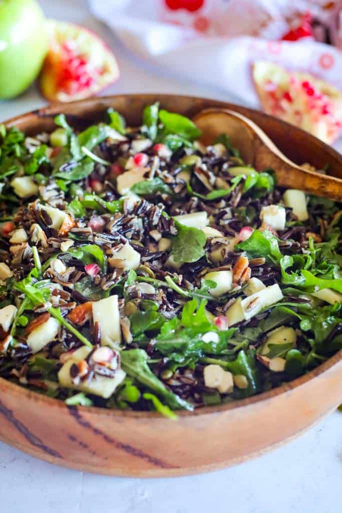 close up of a bowl of wild rice salad with pomegranates in the background