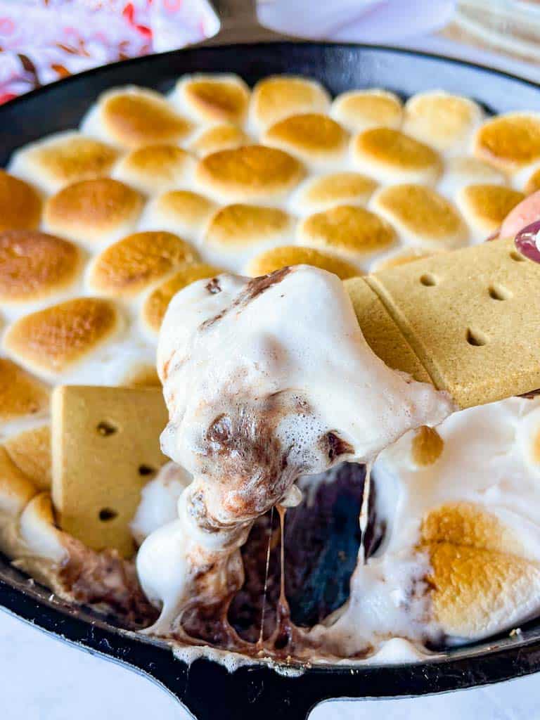 a graham crackers covered in smores dip with a skillet full of the dessert in the background