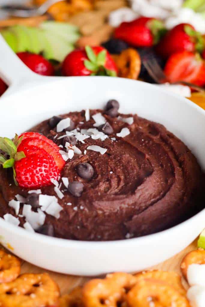 chocolate hummus in a white dish surrounded by pretzels orange slices strawberries sliced apples blackberries and crackers for dipping into the hummus