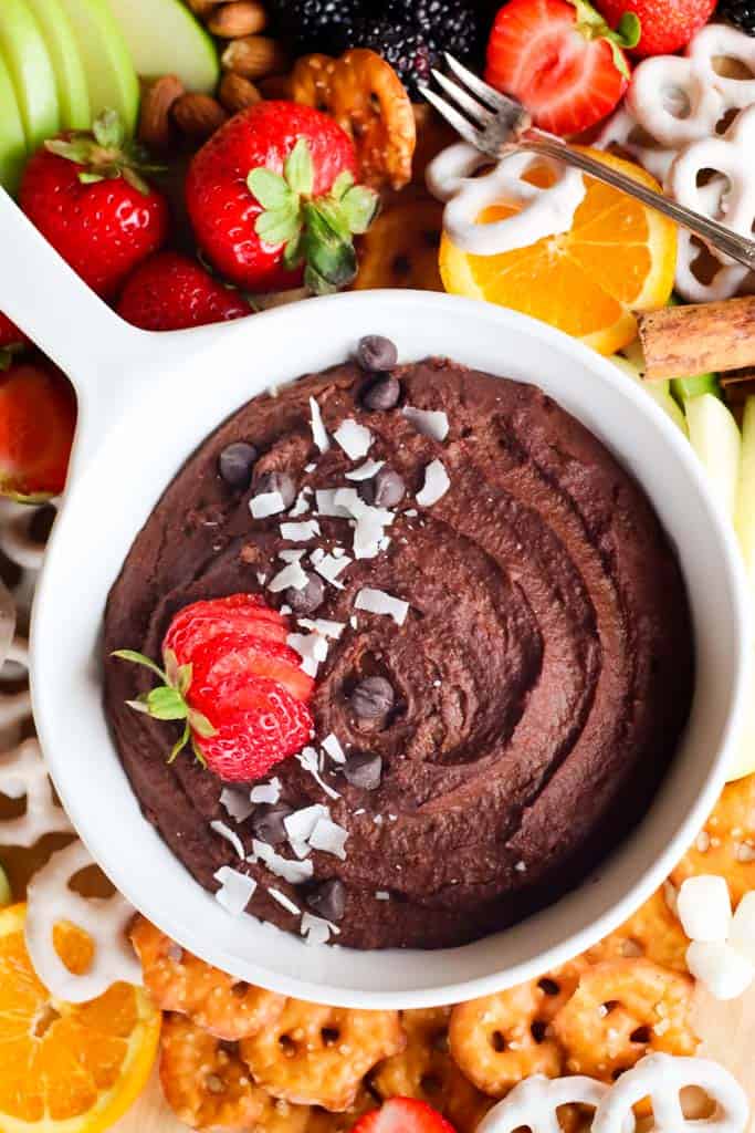 chocolate dessert hummus in a white dish surrounded by pretzels orange slices strawberries sliced apples blackberries and crackers for dipping into the hummus