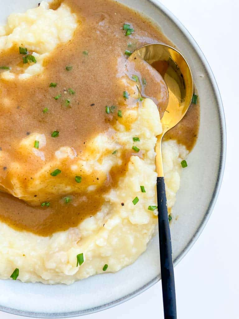 gluten free gravy on mashed potatoes in a white bowl with a gold spoon in the bowl