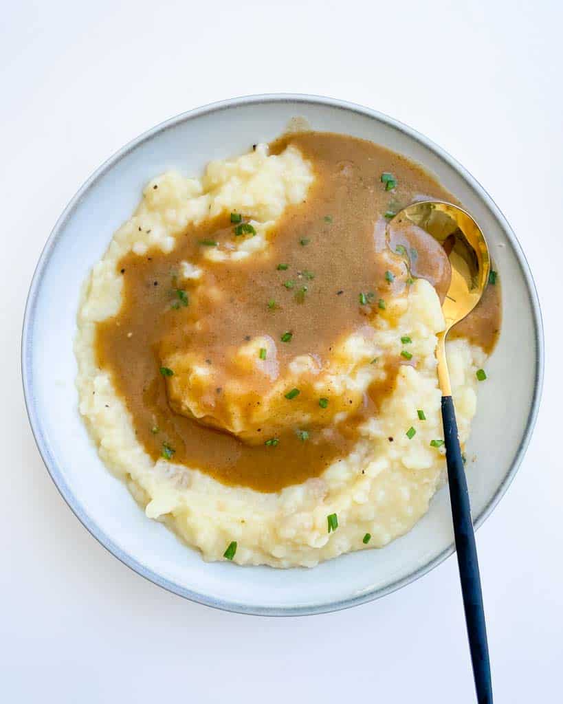 gluten free gravy on mashed potatoes in a white bowl with a gold spoon in the bowl