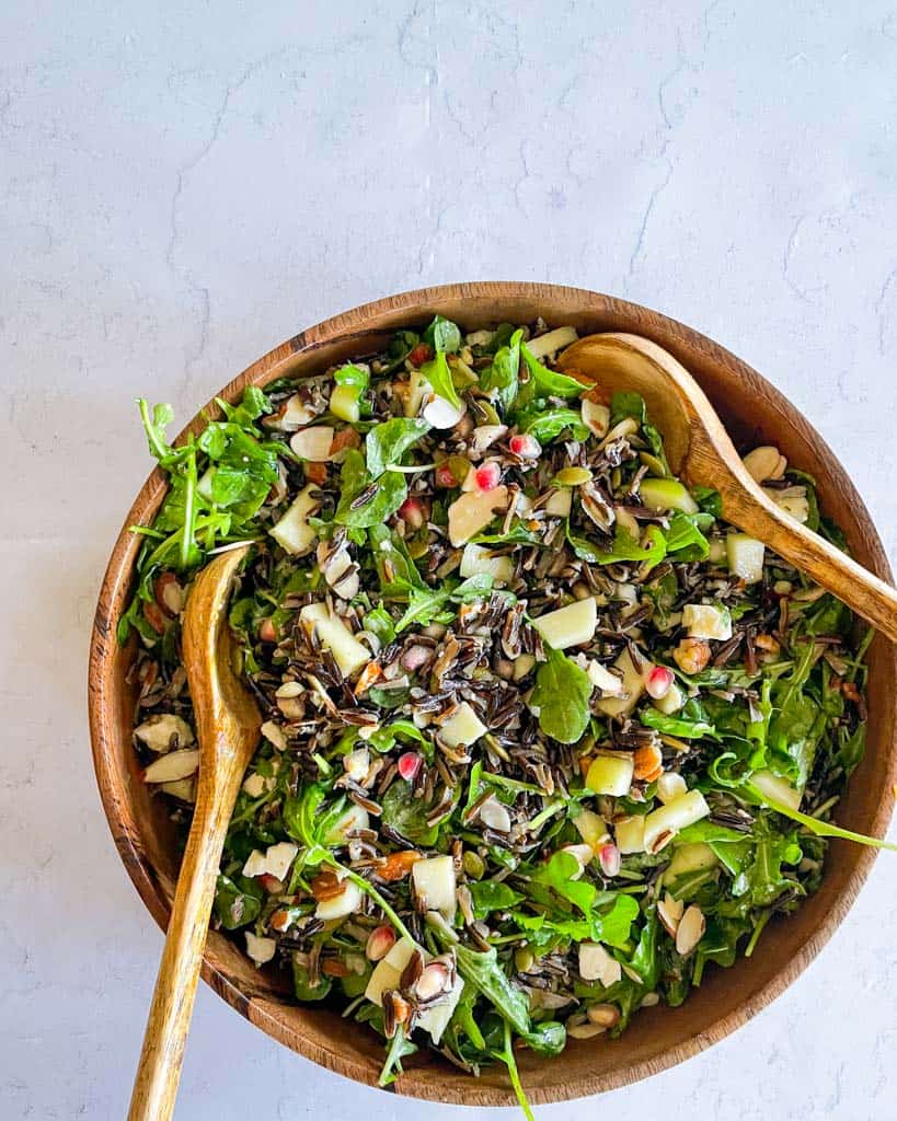 two wooden spoons in a bowl full of wild rice salad