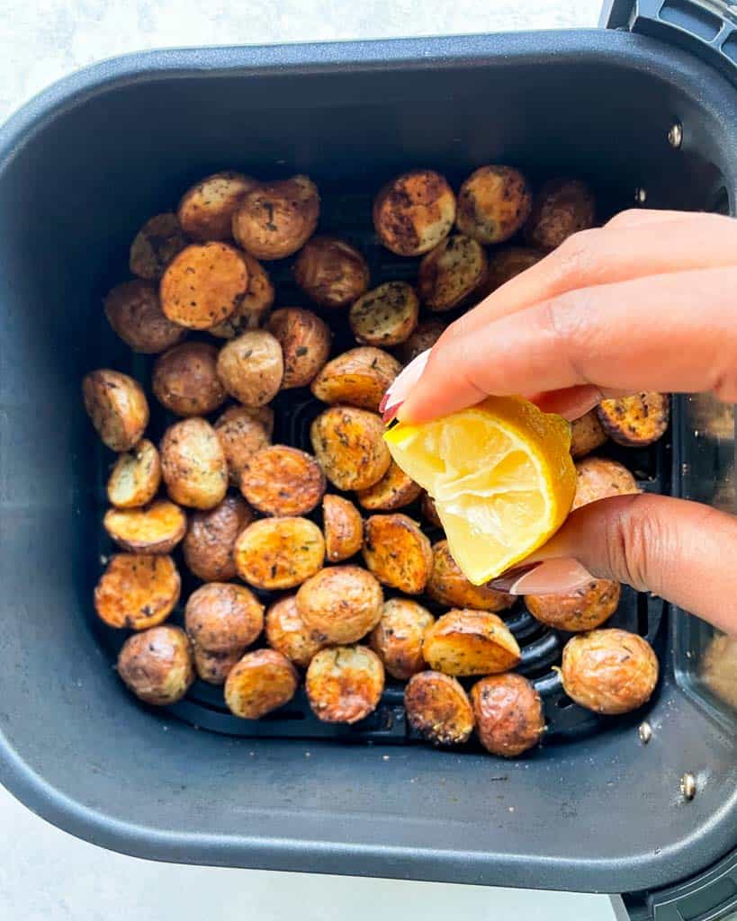 squeezing lemon wedge over baby potatoes in the air fryer