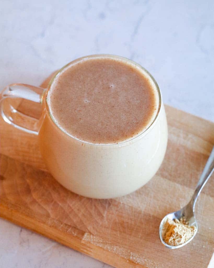 clear mug of maca coffee on a cutting board with a small spoon of maca powder on the side of the mug