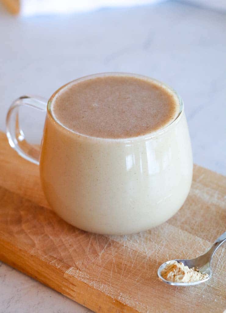 clear mug of maca coffee on a cutting board with a small spoon of maca powder on the side of the mug