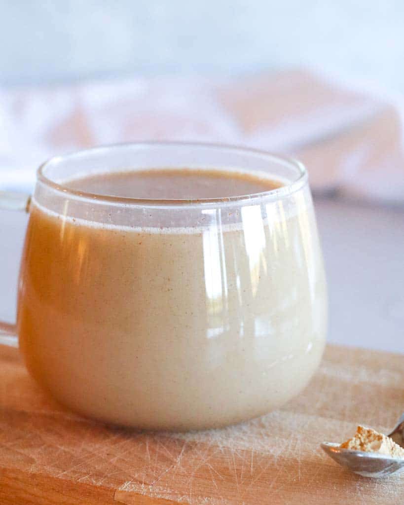 clear mug of maca coffee on a cutting board with a small spoon of maca powder on the side of the mug