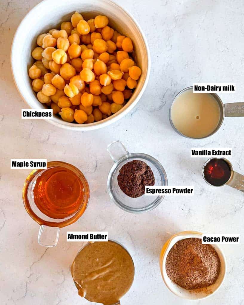 ingredients to make chocolate hummus shown are chickpeas non-dairy mill vanilla extract maple syrup almond butter cacao powder espresso powder